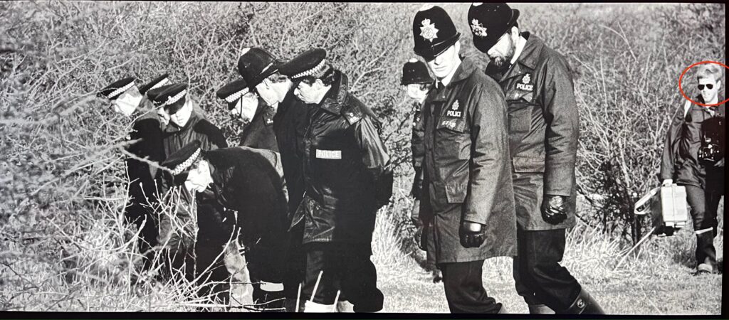 35 Years Later: Reflecting on a Pivotal Case in My Career 4 A black and white photograph from the tv documentary of a line of uniform police officers on Devil's Dyke in February 1990 looking for evidence. Following behind with camera and kit case, Martin Bloomfield