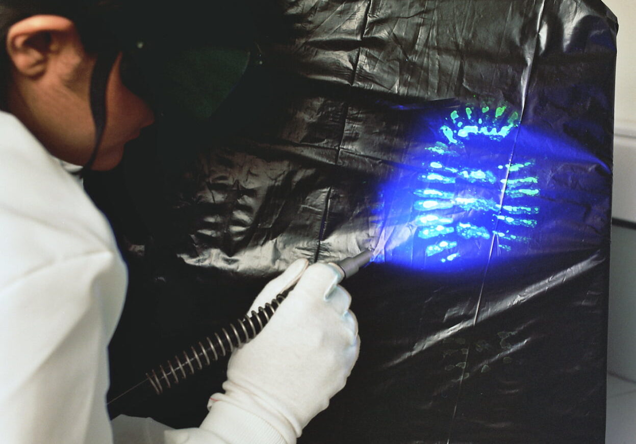 A laboratory technician examines a footwear mark using an alternative light source.